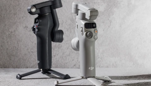 Two smartphone gimbals displayed side by side on a concrete surface, one black on the left and one white/gray on the right.