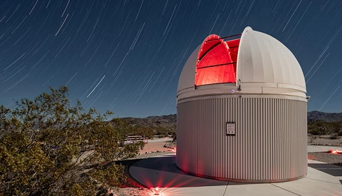 Observatory dome with open slot revealing illuminated red telescope against star trail sky.