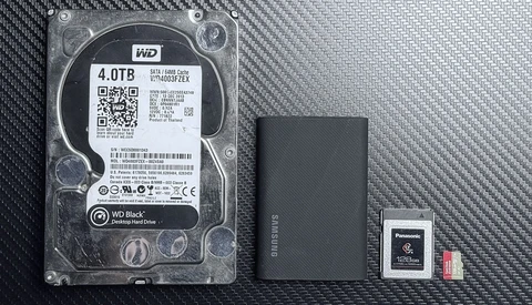 WD Black 4TB hard drive with external SSD, memory card, and microSD card on carbon fiber surface.