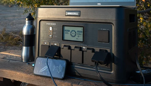 Duracell H2400 portable power station with attached solar panel and charging cable on outdoor wooden surface.