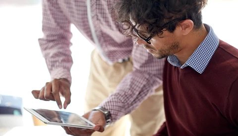 Two people examining a tablet together in an office setting with natural lighting.