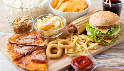 Assorted fast food and snacks arranged on a wooden board and in white bowls.