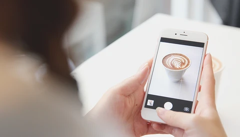 Person holding white smartphone displaying close-up photo of latte art in camera app.