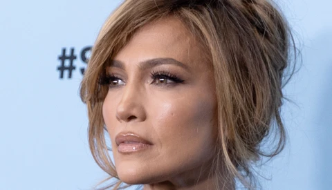 Woman's face in profile against a light blue background, showcasing soft portrait lighting and makeup.