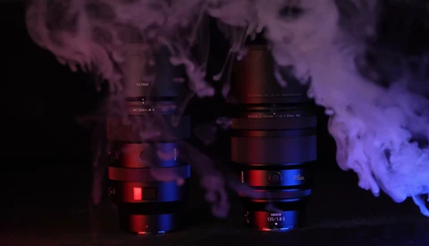 Two camera lenses with red and blue LED lighting creating atmospheric smoke effects against a dark background.