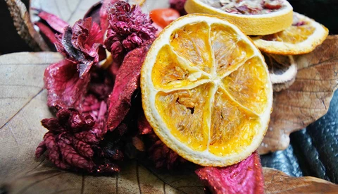 Dried citrus slices and dried flower petals arranged on a wooden surface.