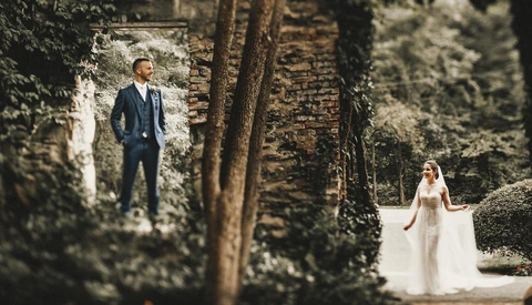 Bride and groom posed separately in an ivy-covered stone passage, bride in foreground wearing flowing white gown.