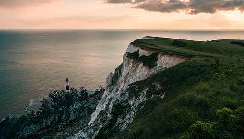 Lighthouse perched on white chalk cliffs overlooking calm sea at golden hour.