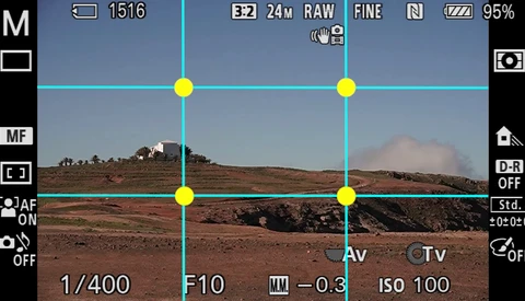 Screenshot of camera viewfinder showing composition grid overlay on arid landscape with distant hills.