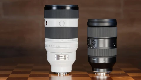 Two telephoto camera lenses side by side on a wooden surface against a brown backdrop.