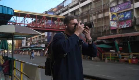 Photographer holding camera to face while standing in urban amusement park setting.