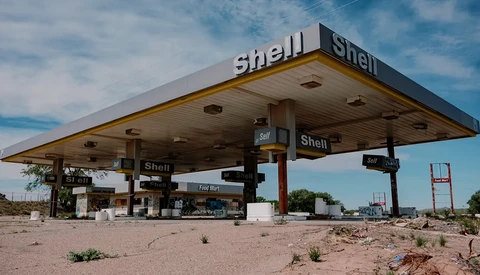Abandoned Shell gas station with weathered canopy under blue sky amid desert terrain.