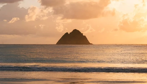 Silhouetted rocky island surrounded by ocean waves at golden hour sunset.