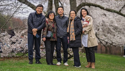 Five people standing together on grass beneath blooming cherry blossom trees.