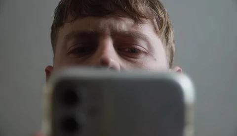 Person holding smartphone up to face, partially obscuring features while looking down at screen.
