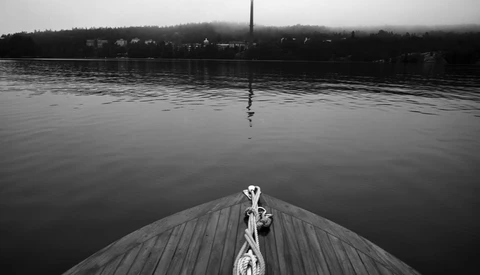 Person standing on wooden dock extending toward calm water with forested shoreline and church spire in background.