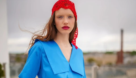 Woman wearing bright blue wrap blouse and red lace headwrap looking over shoulder outdoors.