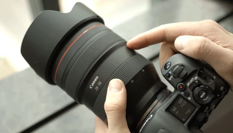 Photographer's hands holding a Canon RF-mount telephoto lens attached to a mirrorless camera body.