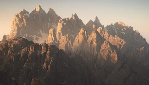 Dramatic jagged mountain peaks bathed in golden sunrise light with deep shadows in the valleys.