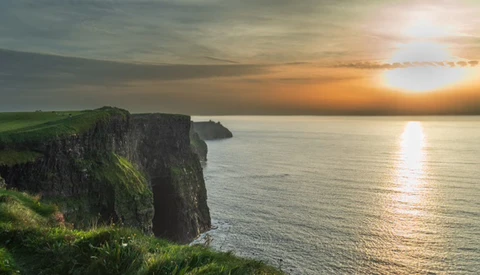 Dramatic coastal cliffs overlooking calm ocean waters at golden hour sunset.