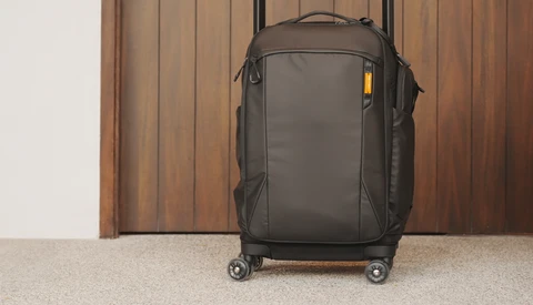 Dark gray rolling carry-on suitcase with spinner wheels against a wooden door and beige carpet.