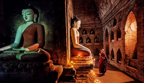 Buddhist statue illuminated in green light inside a candlelit temple chamber with brick walls.