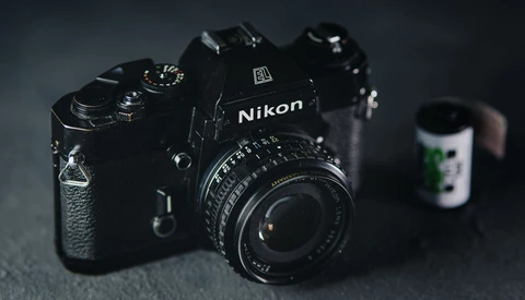 Black Nikon DSLR camera with attached lens on dark textured surface.