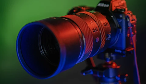 Red telephoto lens mounted on blue camera body against green background with dramatic colored lighting.