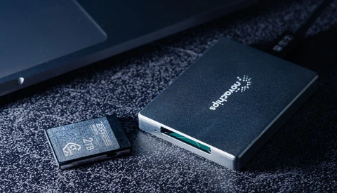 External hard drive and SD memory card on textured dark surface next to laptop.