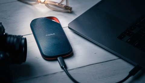 SanDisk portable external hard drive connected to laptop on white desk workspace.