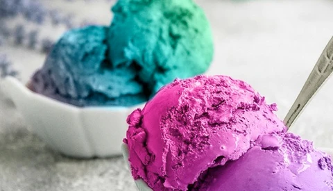 Scoops of vibrant magenta and turquoise ice cream in white bowls with a metal spoon.