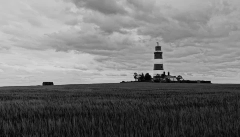 Striped lighthouse standing isolated in a flat, expansive grain field under dramatic cloudy sky.