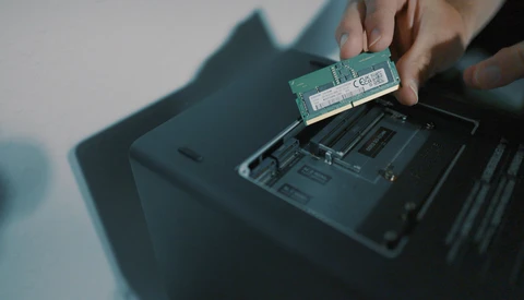 Hands installing a RAM module into a laptop's memory slot.
