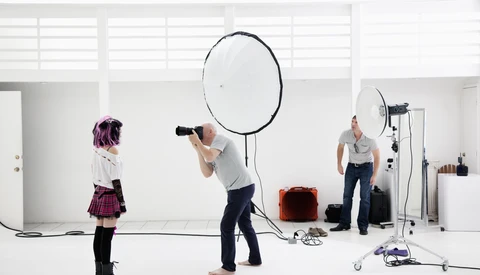 Studio photography setup with model, photographer, and large reflector during a portrait shoot.