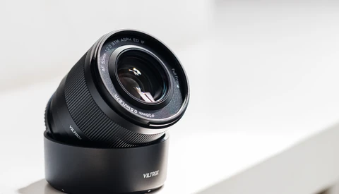 Black telephoto lens with hood mounted on white surface in bright daylight.