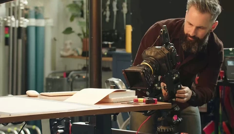 Photographer adjusting a cinema camera mounted on a tripod in a studio setting.
