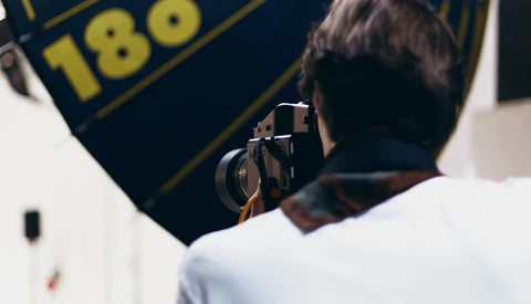 Photographer holding a camera while framing a shot of a navy banner with gold text and numbers.