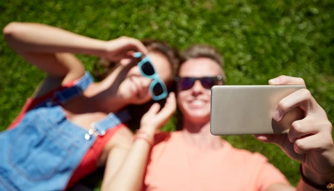 Three people taking a selfie outdoors on grass, with one person holding a smartphone in the foreground.