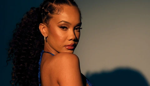 Woman with long curly hair looking over shoulder against blue and warm lighting backdrop.