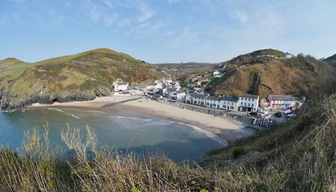 Coastal village nestled in a curved beach cove surrounded by green hills under blue sky.