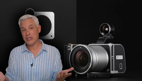 Man in striped shirt discussing camera equipment displayed against black background.