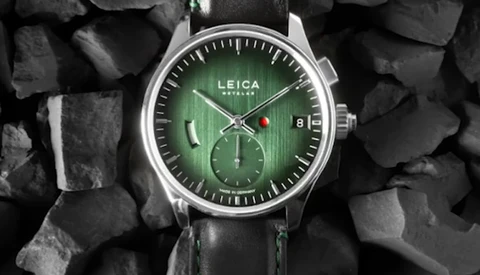Leica chronograph watch with green dial and black leather strap on textured stone background.