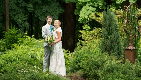 Bride and groom posing together in a lush garden setting with greenery and trees in the background.