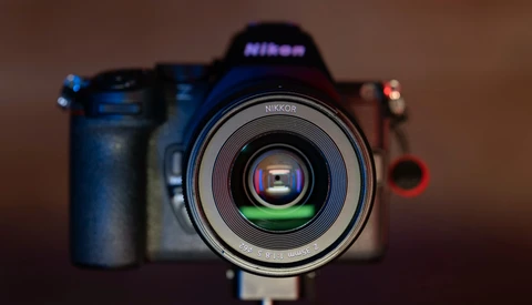 Nikon DSLR camera with Nikkor lens mounted, displayed front-on against a blurred warm-toned background.