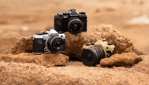 Three mirrorless cameras in different colors arranged on sandy rocks in desert terrain.