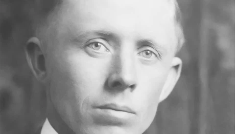 Black and white portrait of a bald man with direct gaze, wearing a collared shirt.