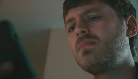 Man with stubble looking downward with concerned expression against neutral background.