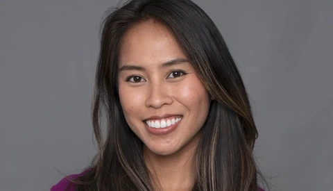 Woman with long dark hair smiling at camera against neutral gray background.