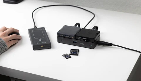 Desktop setup showing a contactless card reader, dual battery chargers, and memory cards on a white desk.