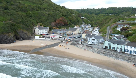 Coastal village nestled between green hillsides and a sandy beach with breaking waves.